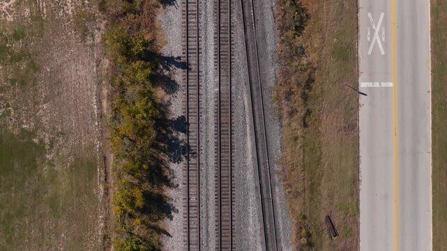 Parallel railroad tracks and roadway crossing open land in Gentry, Arkansas, USA, aerial top-down above electricity utiliy lines