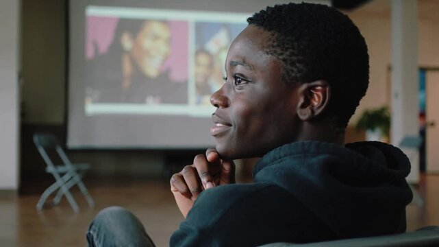 Watching teen in hoodie, jeans propping chin, tapping once following screen starting in room