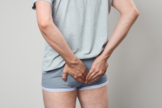 Rear view of man experiencing anal fissure discomfort and proctological pain. Proctologist exam and rectal soreness relief strategy.