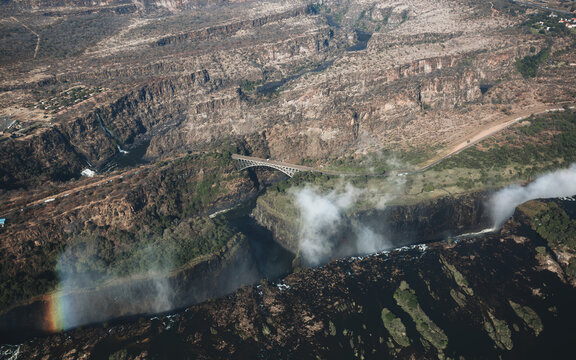Aerial view of the Victoria Falls waterfall, the Victoria Falls Bridge, and the surrounding Zambezi River gorge with mist and a rainbow in Victoria Falls, Matabeleland North Pr, Zimbabwe.