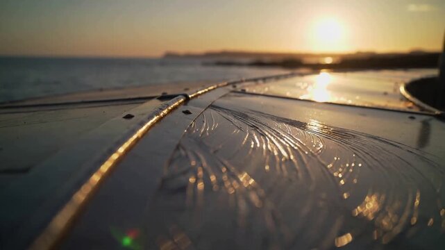Moving camera revealing wet curved boat deck at coast sunset, capturing sun reflections and rivets