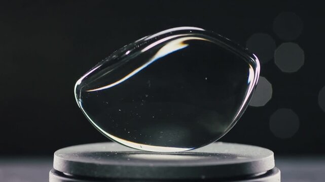 Sequence starting rotating glass droplet showing bubbles and glints at studio with stand and bokeh