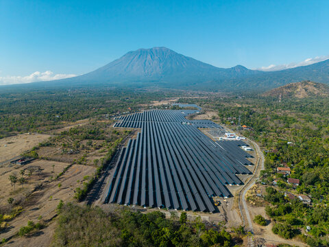 Aerial view of the PLTS Medco Solar Bali Timur solar farm with rows of photovoltaic panels set against the backdrop of Mount Agung in Kubu, Bali, Indonesia.