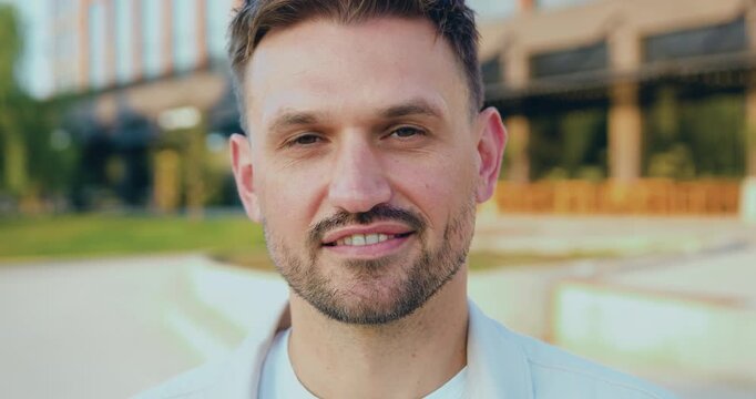 Close-up portrait of a handsome Caucasian man, smiling at the camera outdoors in natural sunlight, people and lifestyle concept.