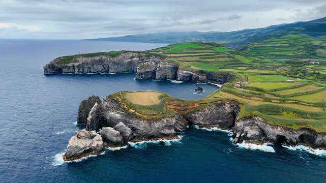 Volcanic headland on Sao Miguel, Azores, rises from Atlantic Ocean with steep rocky cliffs. Wide aerial footage of rugged island coast and coastal geology