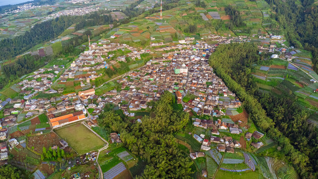 Aerial view of Kaliangkrik village in the mountainous landscape of Central Java, with dense houses surrounded by terraced fields and lush vegetation. Kaliangkrik, Central Java, Indonesia.