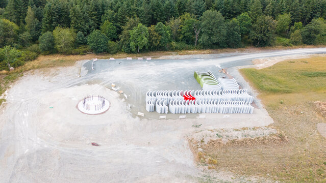 Aerial view of a wind turbine construction site with a circular foundation and rows of curved concrete tower segments on gravel ground in Trier-Saarburg, Rhineland-Palatinate, Germany.