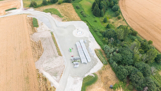 Aerial view of construction site for a wind turbine farm with concrete tower segments on gravel ground surrounded by fields and forest in Trier-Saarburg, Rhineland-Palatinate, Germany.