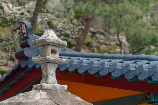 A traditional miniature stone lantern standing on a stone wall with Korean tiled roof in a Buddhist temple.