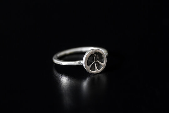 A silver ring featuring a peace symbol on a black background. The ring has a simple design and a polished finish, emphasizing the peace motif.