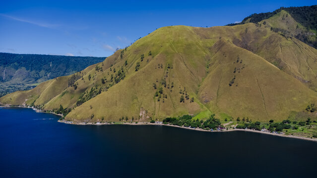 Aerial view of Lake Toba with its grassy hills, calm blue water, and clear sky in Paropo, Sumatera Utara, Indonesia.