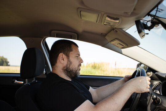male driver struggles to stay awake behind the wheel with drooping eyes and both hands on the steering wheel, illustrating microsleep danger, accident risk and road safety