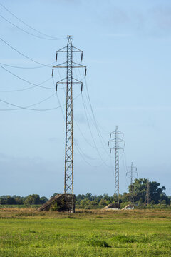 High voltage power lines and steel lattice transmission towers standing in a green field under a clear blue sky.