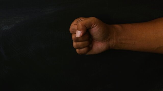 A close up of a human hand clenched into a tight fist against a dark background.