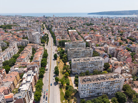 Aerial view of the city of Varna with residential apartment blocks, a long main road with traffic, green trees, and the Black Sea in the background in Varna, Varna, Bulgaria.