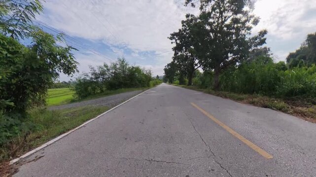Hyperlapse footage traveling along a scenic rural road surrounded by green fields and vegetation, with distant mountains beneath a partly cloudy sky.