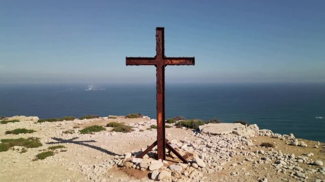 Pulling back camera revealing cliff-top coastline to expose rusted metal cross, triangular supports