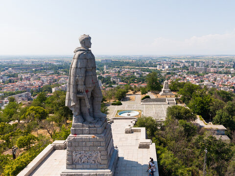 Aerial view of the Monument of the Red Army Alyosha standing on a hilltop overlooking the city, surrounded by lush trees and a paved plaza in Plovdiv, Plovdiv, Bulgaria.