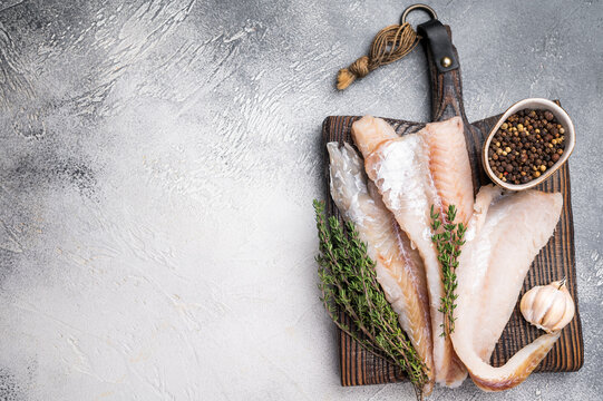 fresh Raw Pollock fish fillets on a wooden board with herbs. white background. top view