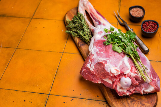 Whole raw lamb leg, uncooked mutton meat on butcher board. orange background. top view
