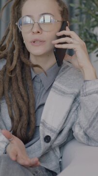 Beautiful young lady with dreadlocks speaking on mobile phone sitting on sofa in luxurious apartment in living room. Communication and cellphone concept.