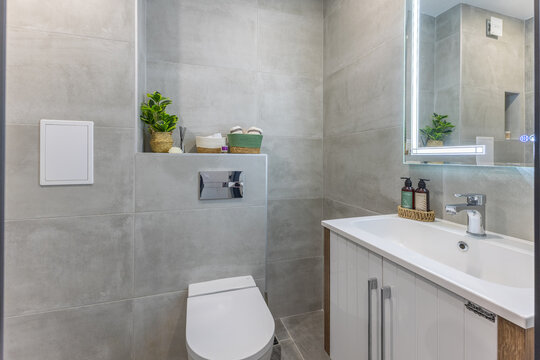 Modern Bathroom Interior with Gray Tiles, Wall-Hung Toilet and Illuminated LED Mirror. Clean Minimalist Home Decor.