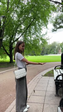 young woman feeds a great tit from her open palm beside a park bench as the wild bird perches close and takes food, illustrating trust, gentle interaction and connection with nature