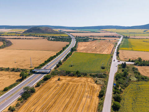 Aerial view of a highway intersection surrounded by golden wheat fields and green agricultural land in the rural countryside Devnya, Varna, Bulgaria.