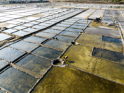 Aerial view of salt pans with workers harvesting salt in the shallow pools under bright sunlight in Moheskhali Upazila, Chittagong Division, Bangladesh.