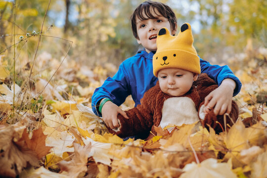 Two children are sitting in yellow leaves in the park for a walk. Family autumn walk in the evening in the park with children.