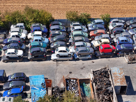 Aerial view of an end-of-life vehicles car scrapyard with rows of stacked cars and metal scrap containers in Spinetta Marengo, Piedmont, Italy.