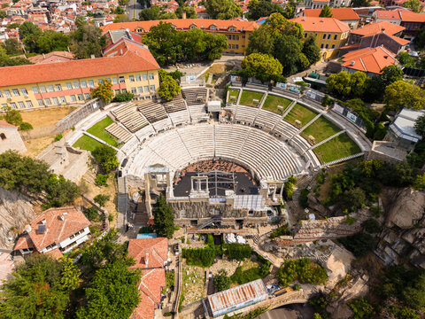 Aerial view of the well-preserved Roman Ancient Theatre of Philippopolis surrounded by historic buildings, lush trees, and stone ruins in Plovdiv, Plovdiv, Bulgaria.