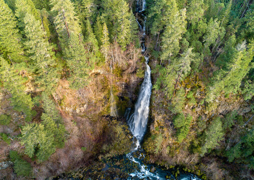Aerial view of Barr Creek Falls cascading down a rocky cliff surrounded by dense evergreen forest in Prospect, Oregon, United States.