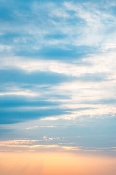 A vertical sunset sky with warm peach glow at the bottom fading into soft blue above. Thin horizontal clouds catch the last light creating layered pastel tones. Perfect for wellness branding.