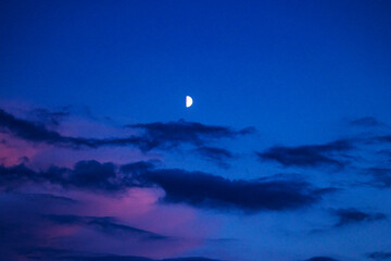 A half moon against the backdrop of a dark evening sky with clouds over the sea © Oleksandr Davydenko