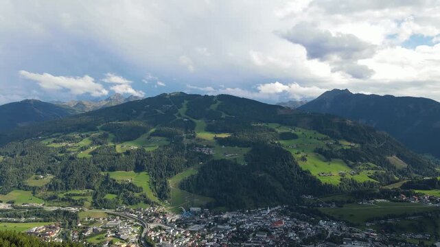 Aerial drone view of Planai mountain and the town of Schladming in the Austrian Alps. Summer sunlight illuminates the alpine landscape while dark storm clouds gather over the mountains