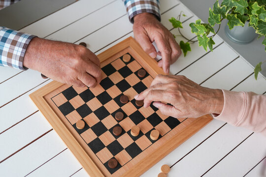Senior adults engaging in a stimulating game of checkers, hands moving pieces on the wooden board, enjoying leisure time and a mental challenge together