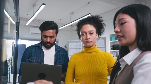 Creative businesswoman brainstorming and writing project strategy on a clear glass board with a marker while her colleague watches carefully.