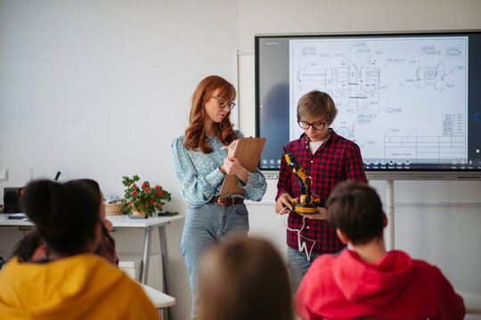 Teen boy explaining robotics project during science and technology class.