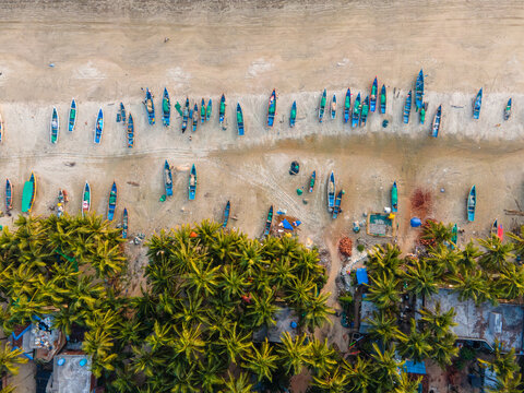 Aerial view of colorful fishing boats lined up on the sandy beach near lush palm trees in Sindhudurg, Maharashtra, India.