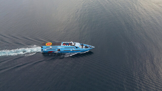Aerial view of a blue passenger ferry boat cruising through the calm dark waters near Waisai Harbour, leaving a white wake behind in Raja Ampat, Papua Barat Daya, Indonesia.
