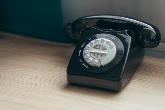 Vintage Black Rotary Telephone On Wooden Desk. Classic Communication Device With Dial Buttons And Glossy Finish.