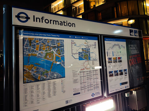 Information board with maps and transport details at Tower Pier on the River Thames in London, UK illuminated at night for visitors and commuters