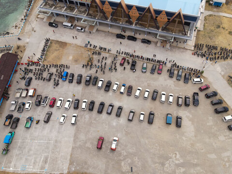 Aerial view of Waisai Harbour terminal building with a large parking lot filled with numerous cars and motorcycles in Raja Ampat, Papua Barat Daya, Indonesia.