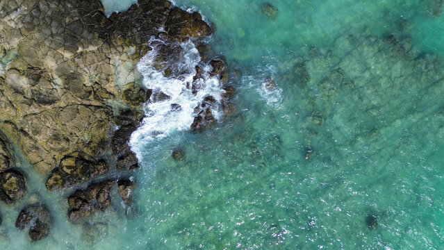 Aerial view of Tanjung Aan Beach with turquoise water and waves crashing against rocky formations in Central Lombok Regency, West Nusa Tenggara, Indonesia.