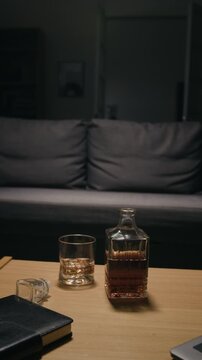 Vertical video showing whiskey decanter, alcohol glass, and notebook on table. Clip suits projects focusing on alcohol addiction, substance abuse awareness, and mental health recovery