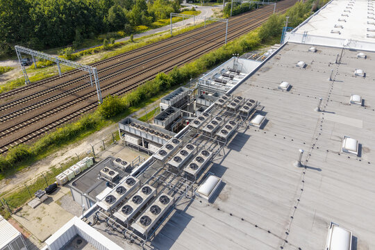 Aerial view of an AI data center cooling system with multiple industrial fans installed on a flat roof, situated next to railway tracks and green vegetation in Poland.