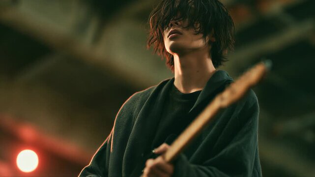 ステージ照明の下でエレキギターを演奏する黒髪の人物