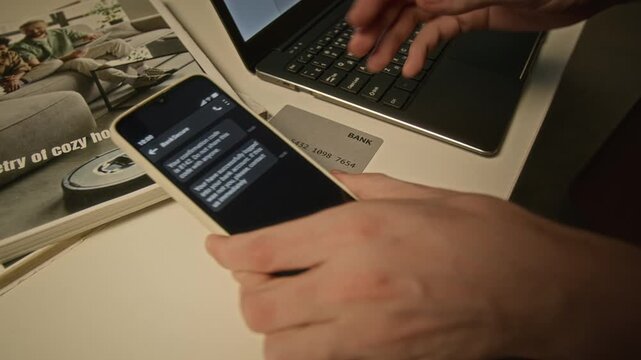 Unrecognizable man typing on laptop keyboard and checking bank confirmation code on smartphone screen. Visual depicts cybersecurity, online transaction safety, and two-factor authentication