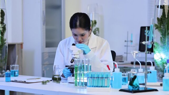 Young Asian female biochemist working with a microscope and developing organic cosmetics and medicine in a professional biotechnology research laboratory with test tubes